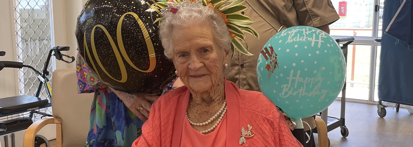 Lady in pink smiles at the camera with birthday balloons in the background 